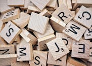 A collection of wooden Scrabble tiles with letters and numbers stacked randomly.